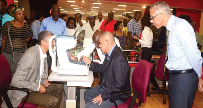 Managing Director of Courts Guyana Ltd, Clyde DeHaas having his eyes tested by Health Minister, Dr George Norton,
while Minister of Business Dominic Gaskin looks on