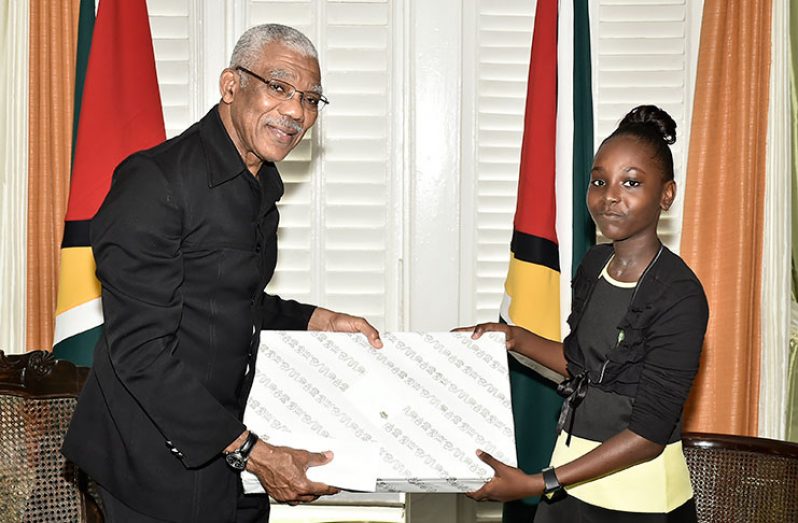 President David Granger presenting Ms. Tyra Walks with a laptop computer and a gift voucher for books.