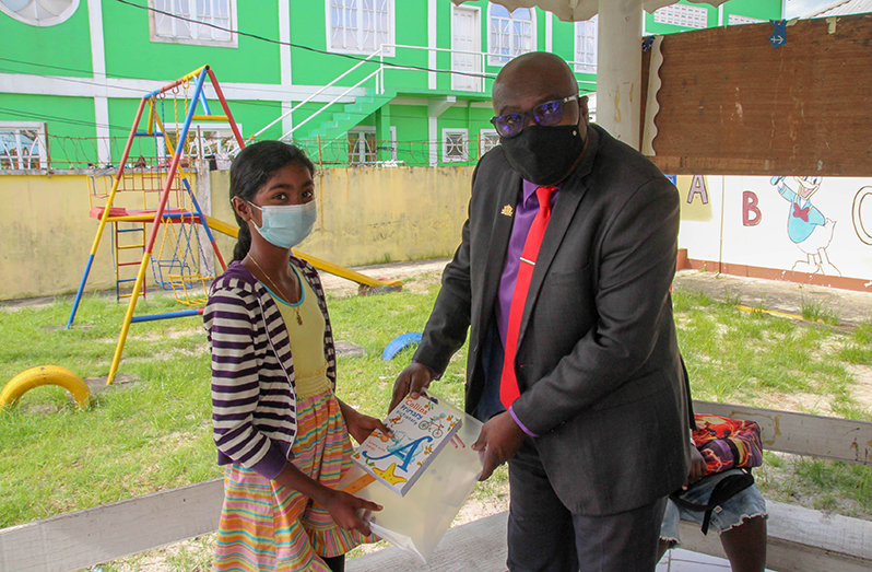 Chief Education Officer, Dr. Marcel Hudson, handing over learning materials to one of the students
