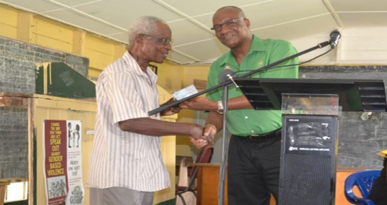 Minister of State Joseph Harmon handing over the cheque to Mr Bowman, resident of Crane Housing Scheme (Ministry of the Presidency photo)