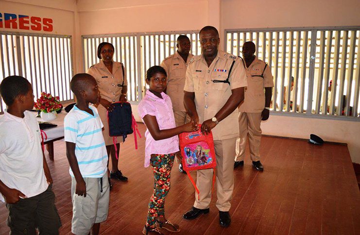 Deputy Commander, Assistant Superintendent Edmond Cooper hands over school supplies to a student, as other students and police officers look on