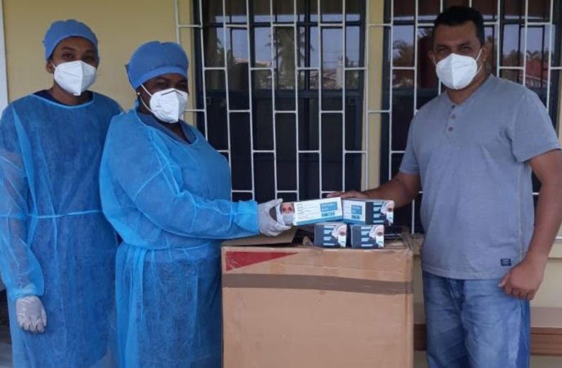 Two frontline workers and Regional Executive Officer, Devanand Ramdatt, with the box of protective supplies, which includes face masks and shields