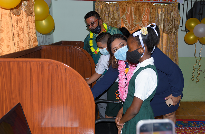 Education Minister Priya Manickchand speaks with nine- year- old Angel Sampson, while Pandit Tillack Shivrattan (left) looks on as 11-year-old Nathaniel Budhu uses one of the laptops (Delano Williams photo)