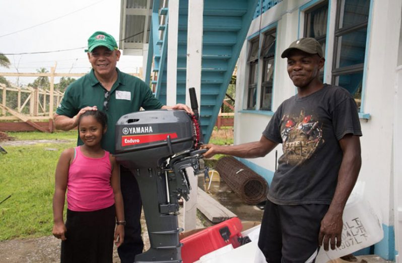 (left to right) Minister of Social Cohesion, Hon. Dr. George Norton, handing over the boat engine to Deputy Toshao, Elvin Evans, along with a student set to benefit from this donation