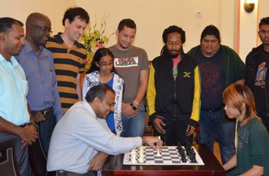 Representatives of the various participating countries observe as Sport Minister Dr Frank Anthony makes the first move against National Junior Champion Haifeng Su to signal the start of the tournament.
