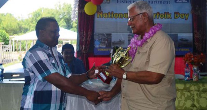Minister of Agriculture Noel Holder hands over a trophy to Ramnarine Ramdharry, the oldest active fisherman, on the occasion of World Fisherfolk Day 2016 on Wednesday.