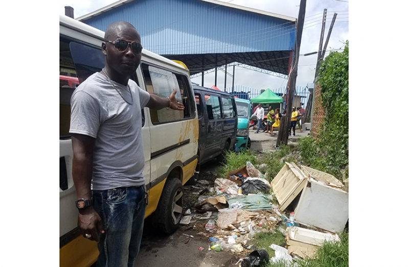 Minibus Driver Bevon Haynes points to a garbage pile next to the bus queue (Tamica Garnett photo)