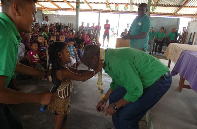 Minister of State Joseph Harmon being garlanded by a young girl on his visit to the South Rupununi village of Achiwuib