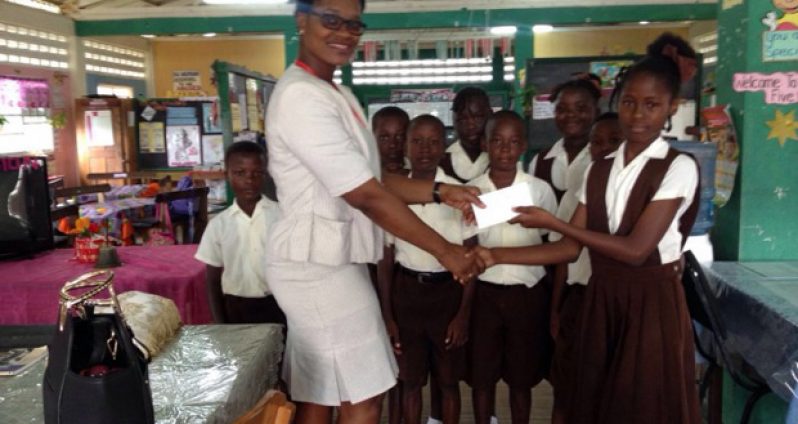 Aurdell Glasgow handing over the cheque to the lead singer of the Den Amstel Primary School Choir, Shania Miller (Ministry of the Presidency photo)