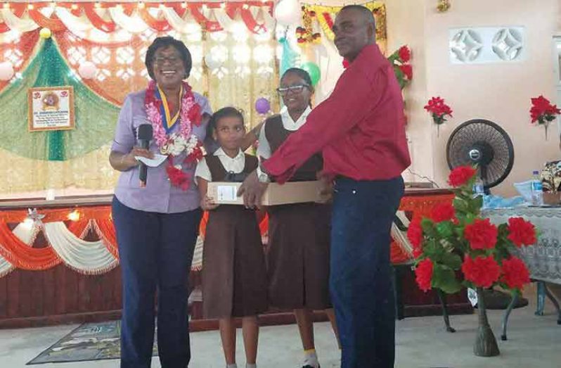 These students receive a computer from Yakusari Community Centre Chairman Mohabir Ramnauth as Minister of Telecommunications Cathy Hughes look on