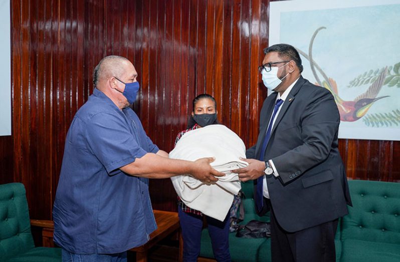 President, Dr Irfaan Ali receives a gift from a resident of Sand Creek during a meeting on Friday (DPI photograph)