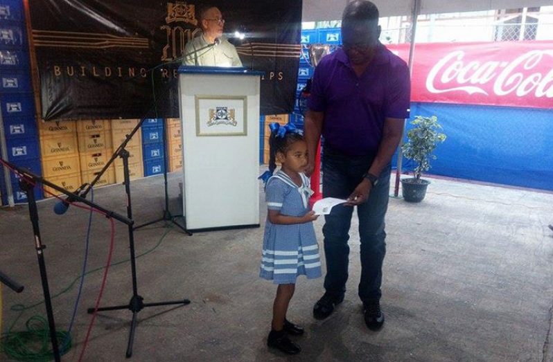 A West Watooka Nursery School pupil receiving a cheque from a company executive at the Banks DIH shareholders meeting last Friday