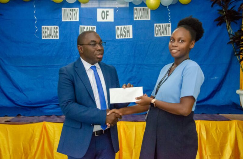 Minister within the Office of the Prime Minister Kwame McCoy handing over the cash grant to a parent in Kuru Kururu on Tuesday. (DPI photo)