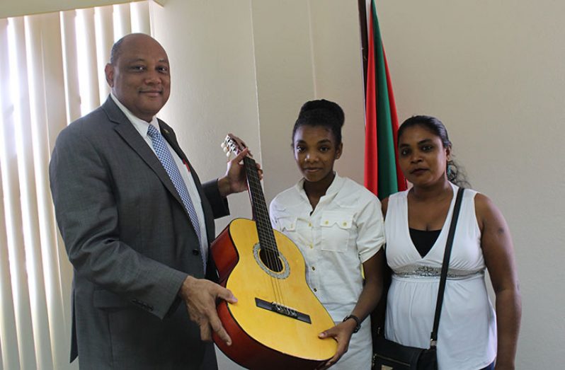 Kanya Miggins receives the guitar from Natural Resources Minister, Raphael Trotman, on Monday in the presence of her mother (Ministry of Natural Resources photo)