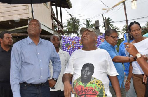 Minister Harmon examining one of the affected homes in the village of Retrieve as the owner makes a point.