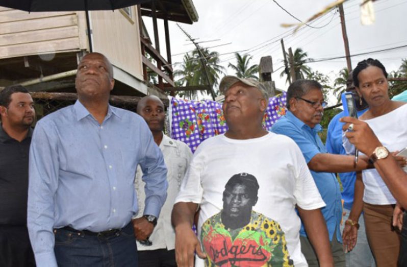 Minister Harmon examining one of the affected homes in the village of Retrieve as the owner makes a point.