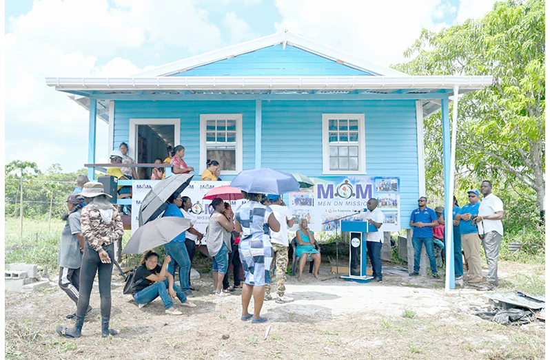 house_ Minister McCoy addresses the small gathering outside the new house which was built through the MoM programme. Also pictured sitting on a chair is the recipient, 80-year-old Dalia Lewis (MoM photo)