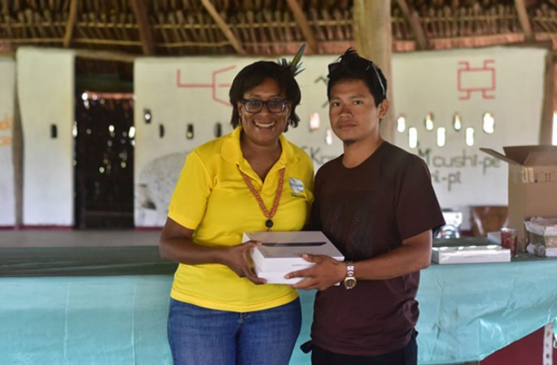 Minister Catherine Hughes hands over a tablet to Brenrick Francis, a youth leader in the Kumu Village