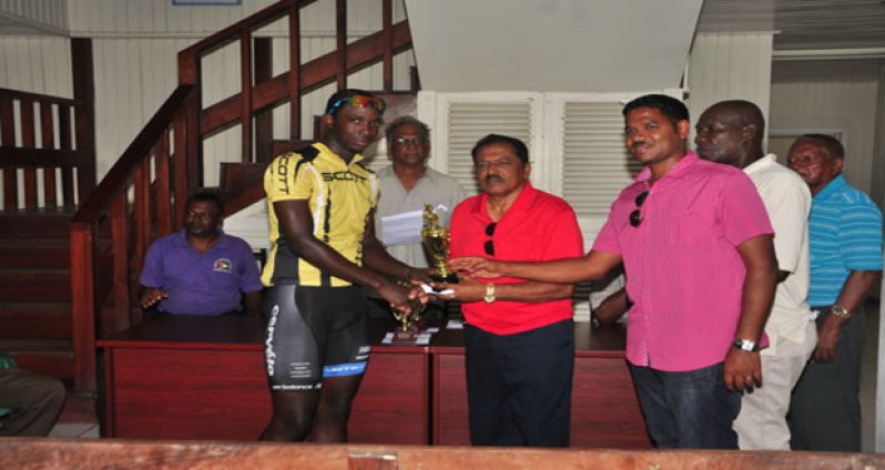 Akeem Arthur (extreme right) accepts his prize for winning the third stage of the Cheddi Jagan Memorial Cycle Race yesterday in Essequibo from stage sponsor Suresh Jagmohan while at centre is Minister within the Ministry of Agriculture Ali Baksh. Looking also is Dirretor of Sport Neil Kumar and National cycling coach Hassan Mohamed.
