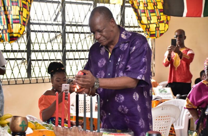 Minister of State Mr. Joseph Harmon lights the 'Umoja' candle, which signifies a commitment to promoting and embracing unity