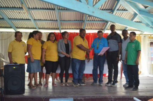 land-title Minister of Indigenous People's Affairs, Sydney Allicock, handing over the land title document to Toshao of the community, Trevor Matheson, in the presence of Permanent Secretary in the Indigenous People's Affairs Ministry, Alfred King; Regional Executive Officer of Region One, Leslie Wilburg; Vice-Chairman of Region One, Sarah Brown and councillors and residents of the Community.