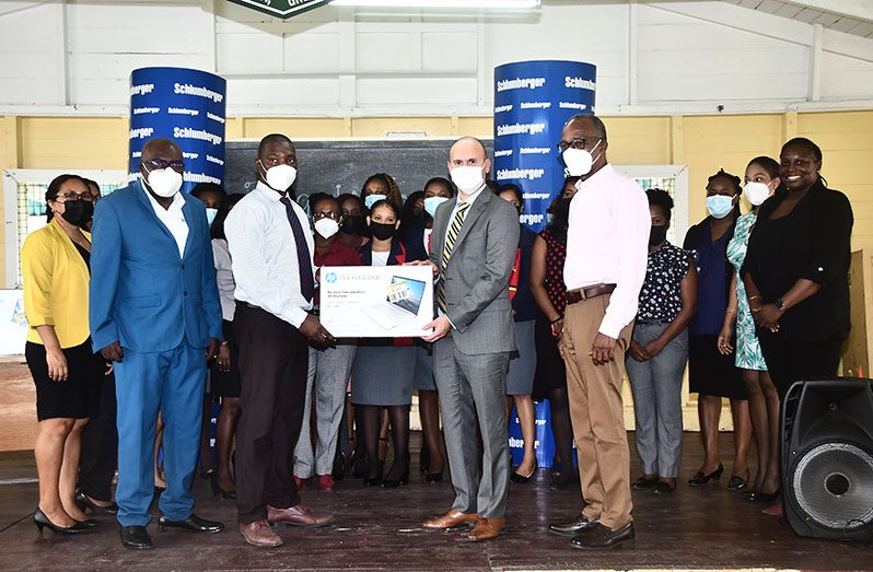 Managing Director of Schlumberger GTC, Ernesto Cuadros hands over one of the 30 laptops to Houston Secondary Headteacher, Kevin Williamson.  Looking on are teachers and Chief Education Officer, Dr. Marcel Hutson (left of Williamson) and Labour Minister, Joseph Hamilton (right of Cuadros)