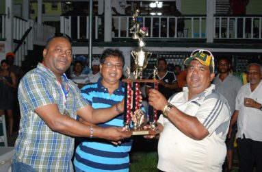 PRESIDENT of Everest Cricket Club Stephen Lewis (left) hands over the winning trophy to manager of New York Blasters, Hafeez ‘Rockaway’ Ali. Sponsor Manniram Shew is at centre.
