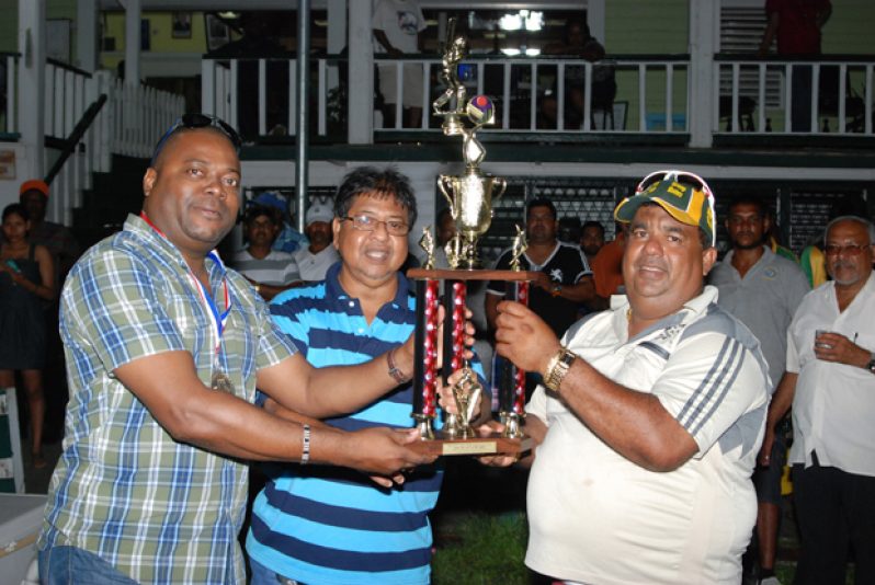 PRESIDENT of Everest Cricket Club Stephen Lewis (left) hands over the winning trophy to manager of New York Blasters, Hafeez ‘Rockaway’ Ali. Sponsor Manniram Shew is at centre.