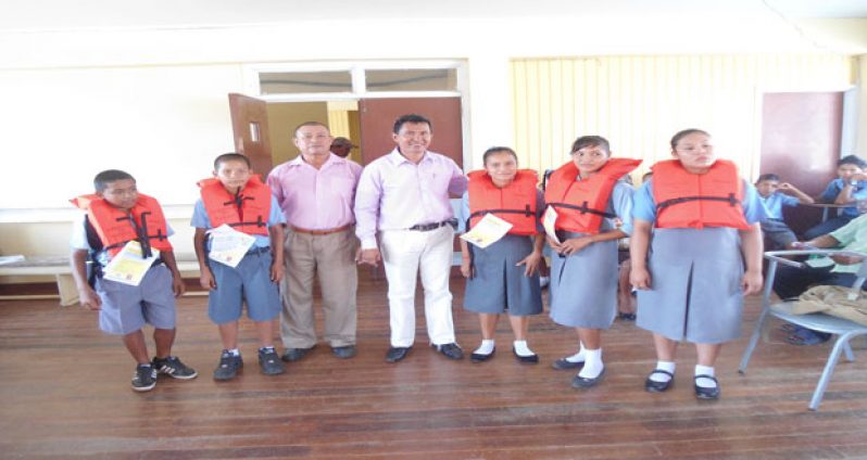 Assistant Regional Executive Officer Gerald Rodrigues and the District Education Officer Ignatius Adams, pose with children after receiving their life jackets.