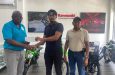 Ian John, left, receives the cheque from Anthony Rahaman Khan while Buddy Rahaman looks on