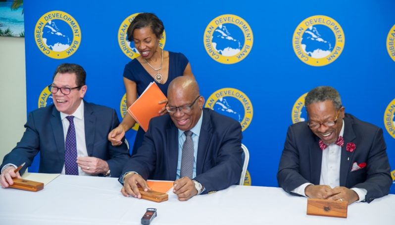 CDB President Dr Warren Smith, Minister of Finance  Winston Jordan and Vice Chancellor of the University of Guyana Professor Ivelaw Griffith at the signing ceremony . 
Assisting is Diana Wilson Patrick (standing), General Counsel, CDB . (Photo credit : CDB)