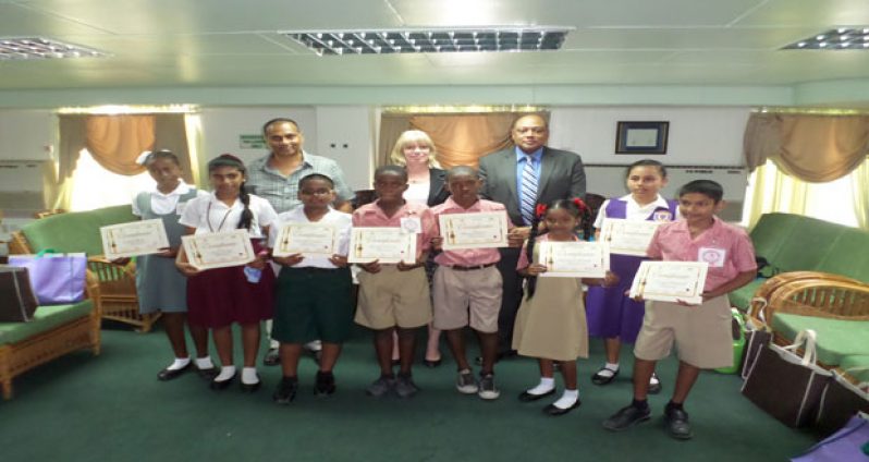 Mr. Philbert Gajadar, UG Art Lecturer; Ms. Merriam Flach, Resident Representative, UNICEF; and Mr. Raphael Trotman, Speaker of the National Assembly pose for a photograph with the winners of the art conatural colourmpetition