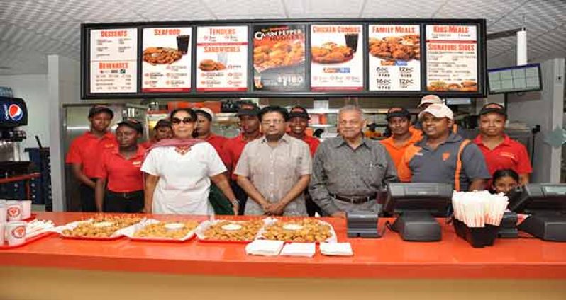 Finance Minister Dr Ashni Singh and Guyana Restaurant Inc Chairman Mr Ram Lallbahadur Singh pose with staffers of the new Popeyes location on Water Street, Georgetown yesterday (Delano Williams photo)