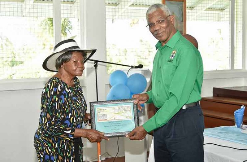 President David Granger, on Thursday, received from Evelyn Bacchus, the oldest resident of Victoria Village, the Village's 177th anniversary commemorate stamp (Ministry of the Presidency photo)