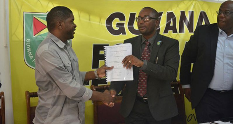 Contractor Dwain Ferdinand collects the inked contract from GFF president Wayne Forde as FIFA development officer Howard McIntosh looks on.