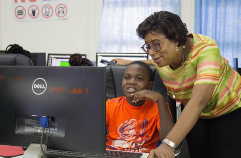 Minister of Public Telecommunications, Catherine Hughes, shows a young lad the steps to operate the computer at an ICT Hub in Linden