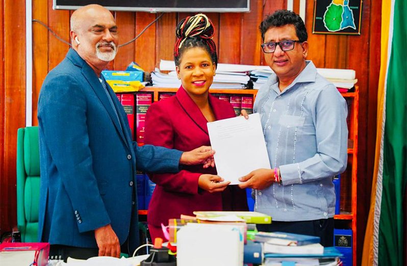 Attorney General, Anil Nandlall, presents a copy of the Draft Real Estate Bill 2023 to Guyana Association of Real Estate Professionals representatives Nicola Duggan (centre) and Komal Ragnauth