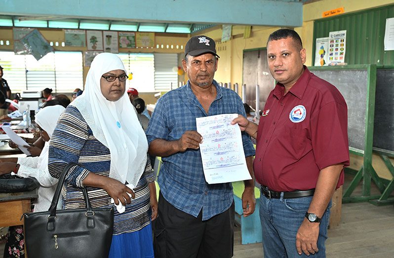 Mohamed Amin Bassir (centre) and his wife (left) being presented their Agreement of Sale by Minister of Housing and Water, Collin Croal