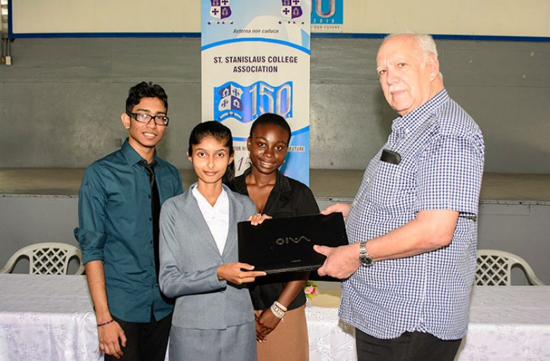 Chairman of the local St. Stanislaus Association Board of Governors Chris Fernandes handing over a laptop computers to the University of Guyana scholarship awardees Shemaka Felix and Arianna Mahase, while Jemuel Parsram and Shemaka Felix stand by. (Photo by Samuel Maughn)
