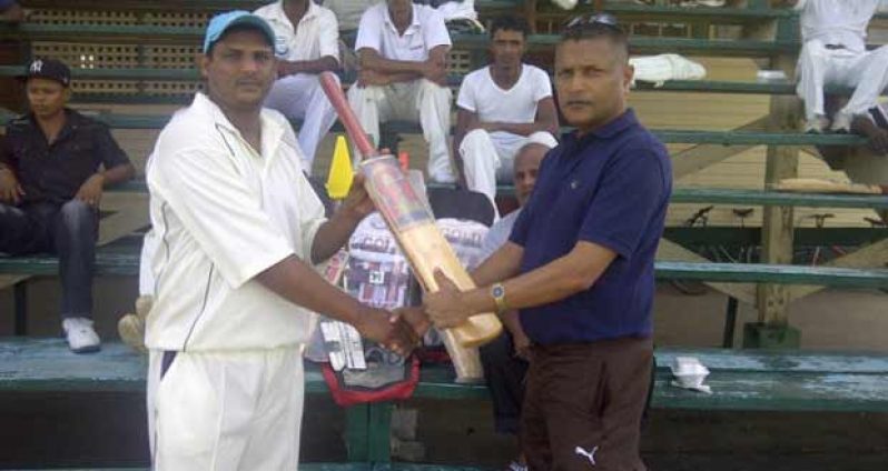 Ramesh Takur left receiving the cricket gear from Anand Sanasie, as other members and well wishers of the club look on attentively in the back ground.