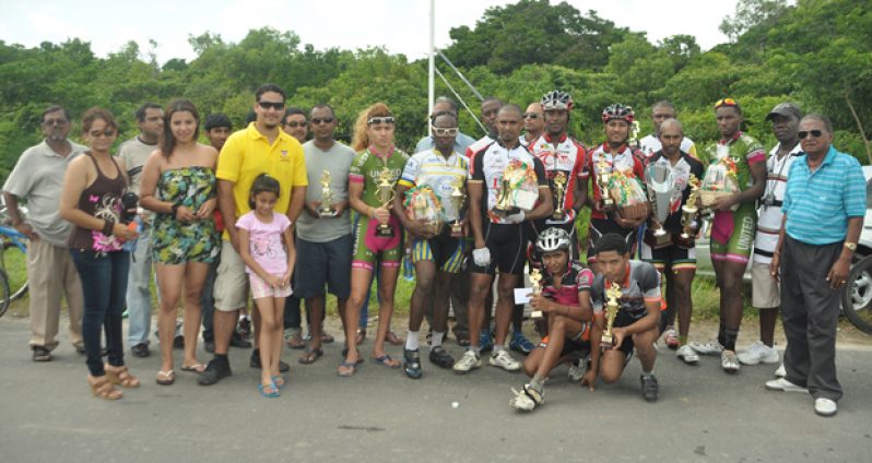 Reagan Rodrigues Jr (third from left standing) and race winner Robin Persaud ((fourth from right with trophy), strike a pose with other category winners after yesterday’s Regaan Rodrigues 10th Memorial 50-mile cycle road race.