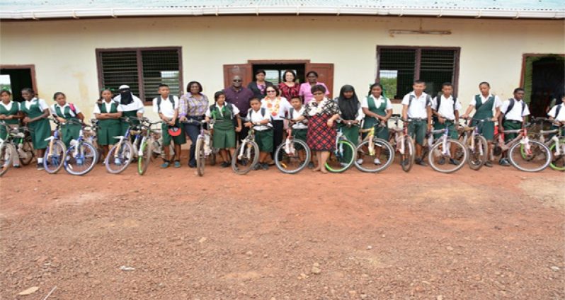 From left: Chief Education Officer in the Ministry of Education, Mr. Olato Sam; First Lady, Mrs. Sandra Granger, Minister of Social Cohesion, Ms. Amna Ally and other officials stand with the beneficiaries who proudly displayed their bikes at the St. Ignatius Primary School
