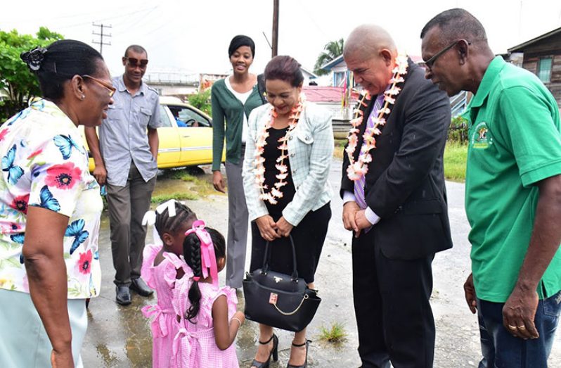 Minister of Social Cohesion, Dr. George Norton and Technical Officer, Ministry of Social Cohesion, Pamela Nauth are being greeted by two nursery school pupils at the Wakenaam, Region Three (Essequibo Islands-West Demerara) NDC