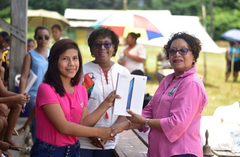 Minister within the Ministry of Indigenous Peoples’ Affairs, Valerie Garrido-Lowe, along with Minister of Public Telecommunications, Catherine Hughes, hands over a tablet to a representative of the sports group at Fairview