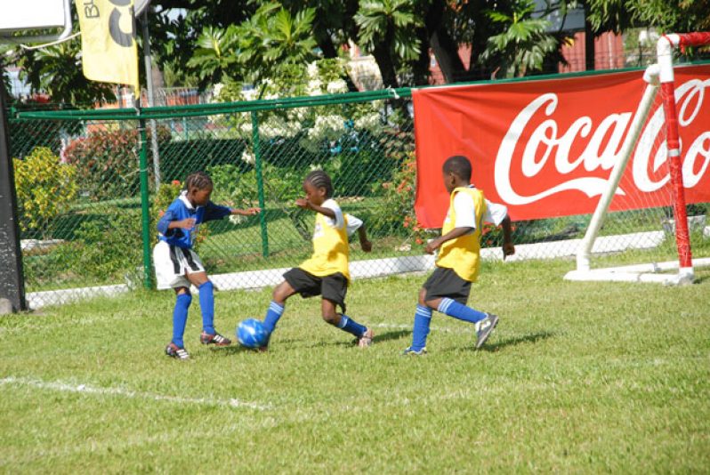 West Ruimveldt’s ace player Michael Oie (blue bib) was captured by Chronicle Sport’s photographer Sonell Nelson just before he weaved his way around these two players from Tucville Primary School, during the two sides’ clash at the Banks DIH, Thirst Park ground yesterday.