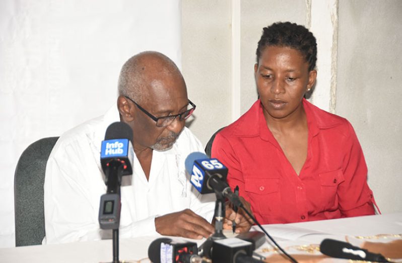 Minister within the Ministry of Social Protection, Keith Scott (left), refers to some of his documents as a representative of GNCUL looks on