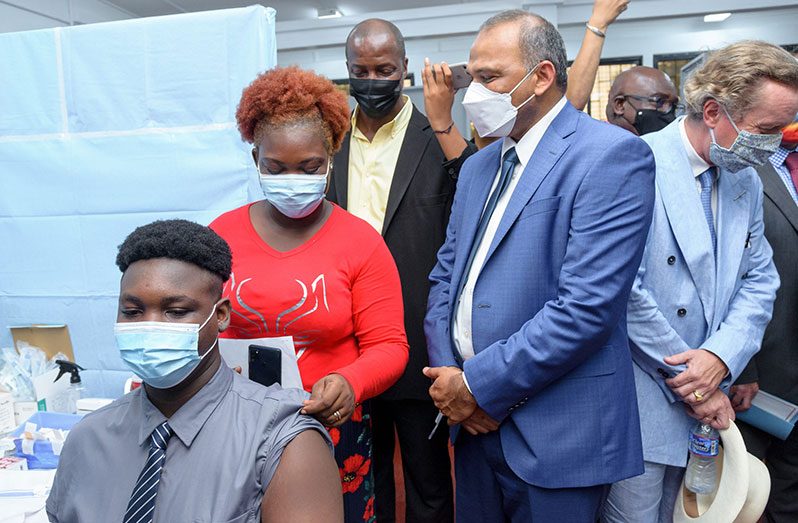 Minister of Health, Dr. Frank Anthony, looks on as 15-year-old Ramon Cummings takes his first dose