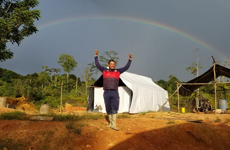The miner at camp raising his hands during a productive day below a rainbow in the sky