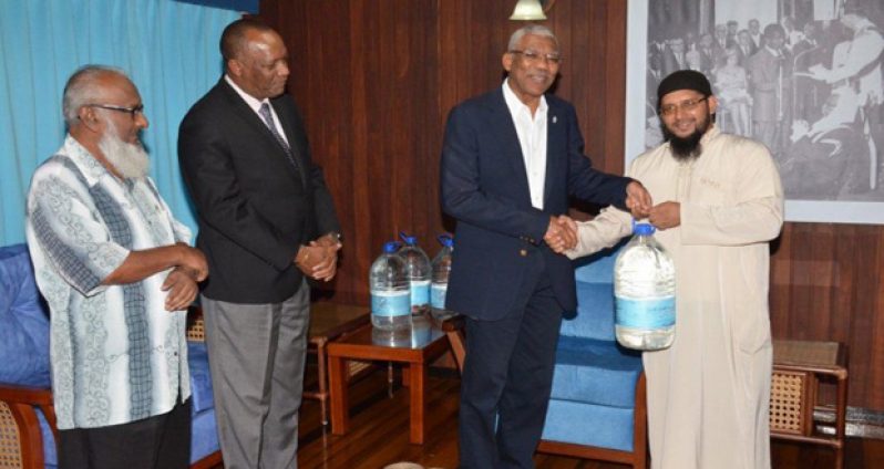 President David Granger shares a warm handshake with Shaykh Abdul Aleem Rahim,
President of the Guyana Islamic Trust, as he presents him with a bottle of Zamzam water,
while Minister of State Joseph Harmon and another representative look on