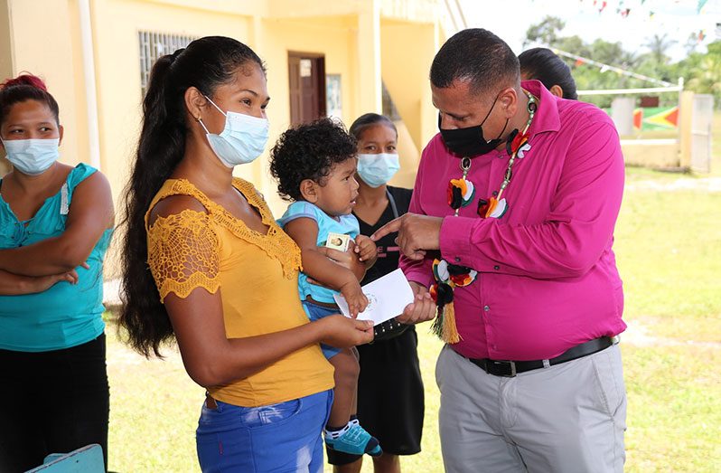 Housing and Water Minister, Collin Croal, hands over a cheque to a mother and her child at the Wauna Primary school